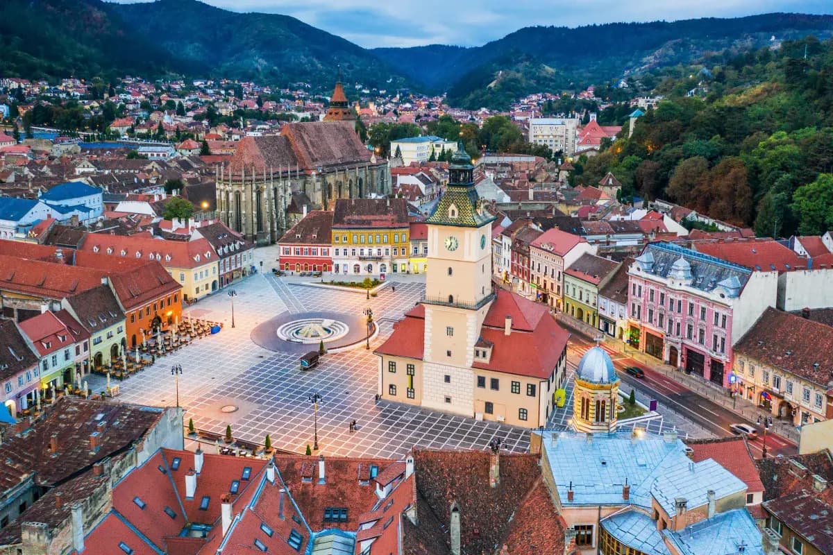 Aerial view of Brașov Council Square with the Black Church, the Council House clock tower, and the Carpathian mountains in the background
